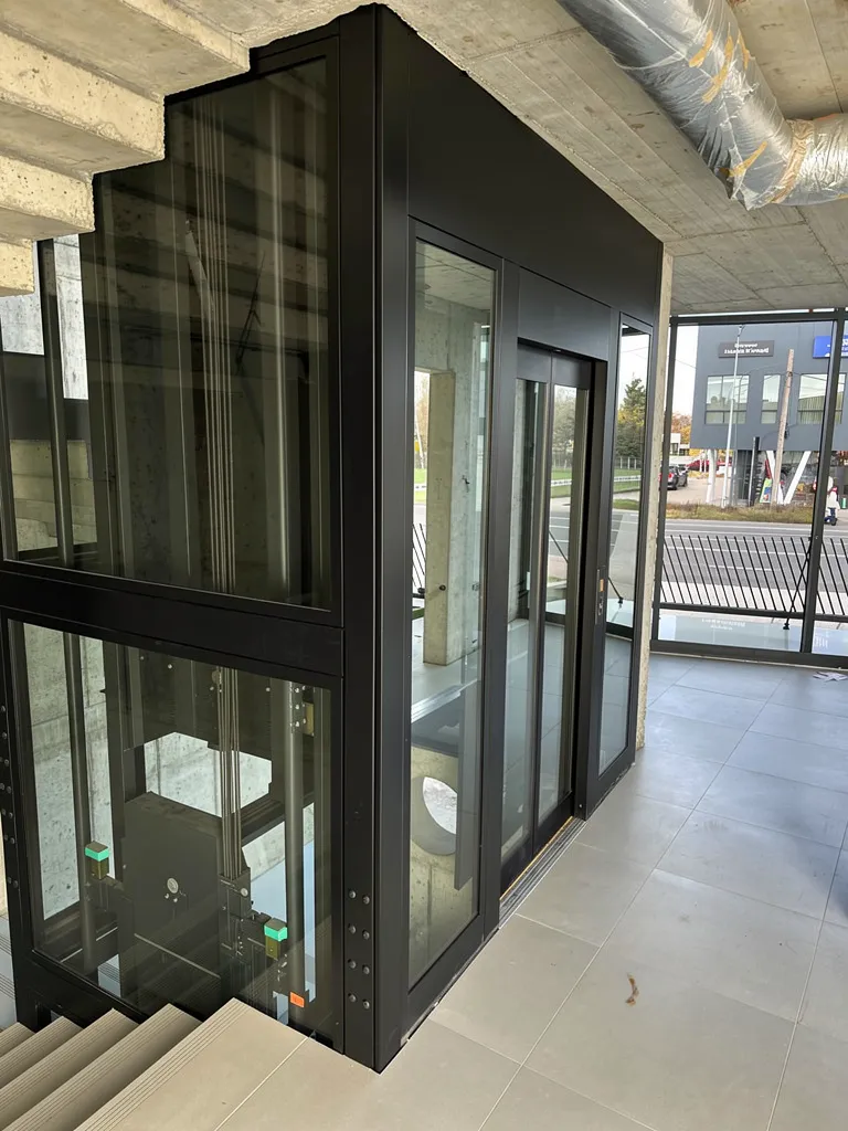 Czarny szyb panoramiczny od zewnątrz przy oknie kondygnacji, widać mechanizm pod kabiną